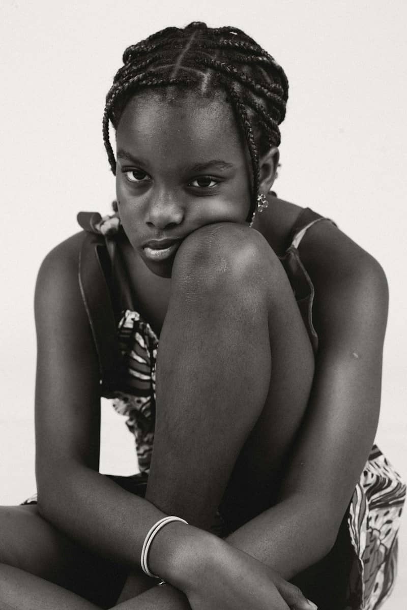 A young girl with braided hair resting her chin on her knee