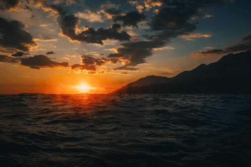 Golden sunset over a dark, wavy ocean with mountains.