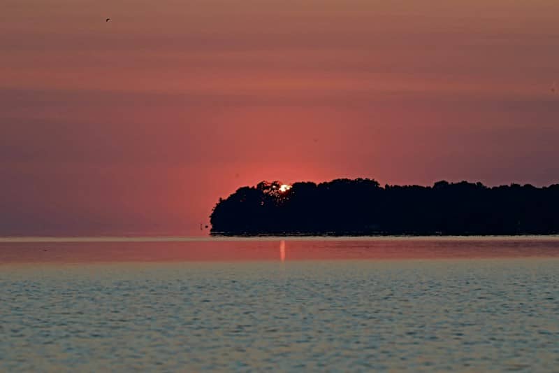 Red sunset over calm water with a dark island.