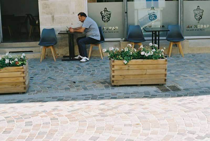 Man at outdoor cafe table with flower planters