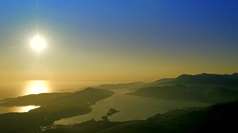 Golden sunset over a bay surrounded by mountains.