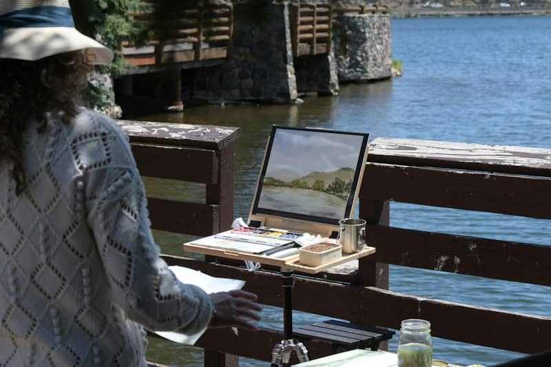 A woman painting a landscape by the water.