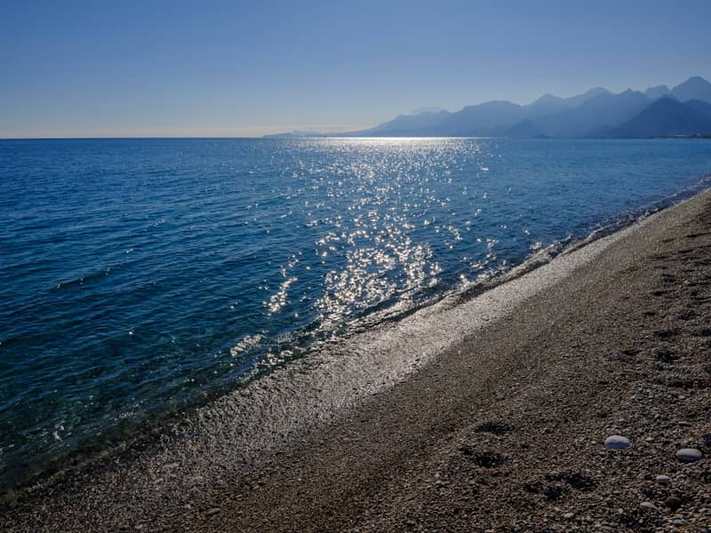 Sparkling ocean and mountains from coastal beach at sunset