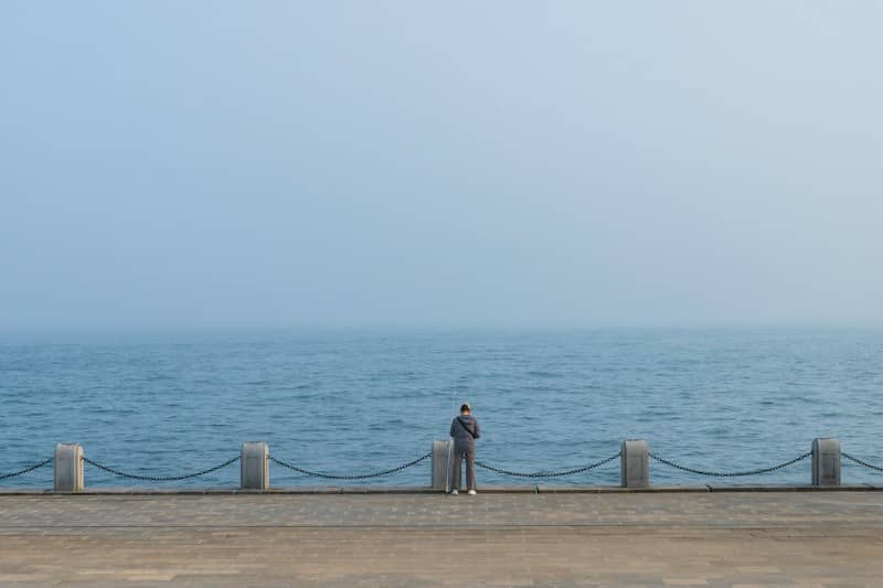 Person overlooking the vast, misty ocean from a concrete pier.