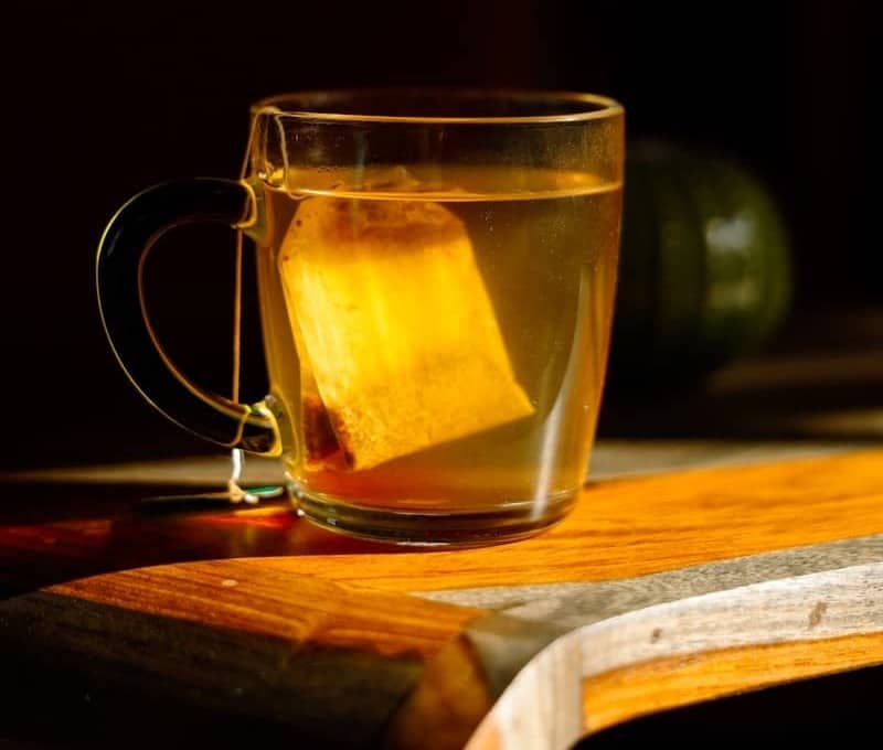 A tea bag steeping in a glass mug.