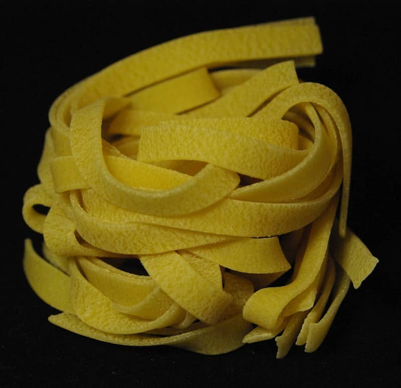 A nest of dried yellow fettuccine pasta on a plain black background