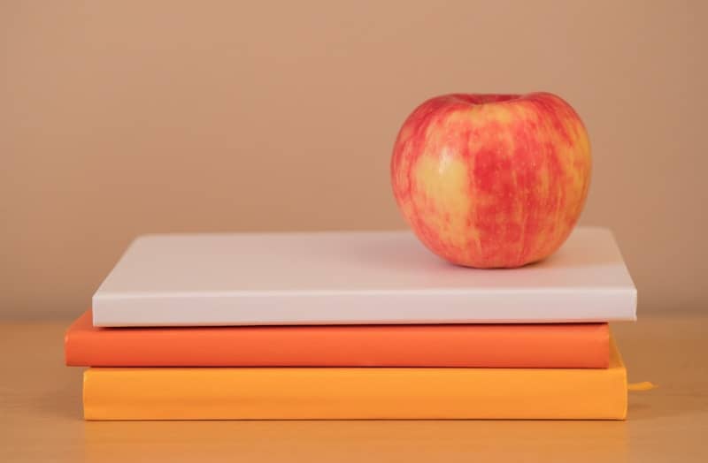 A red and yellow apple on a stack of white and orange books
