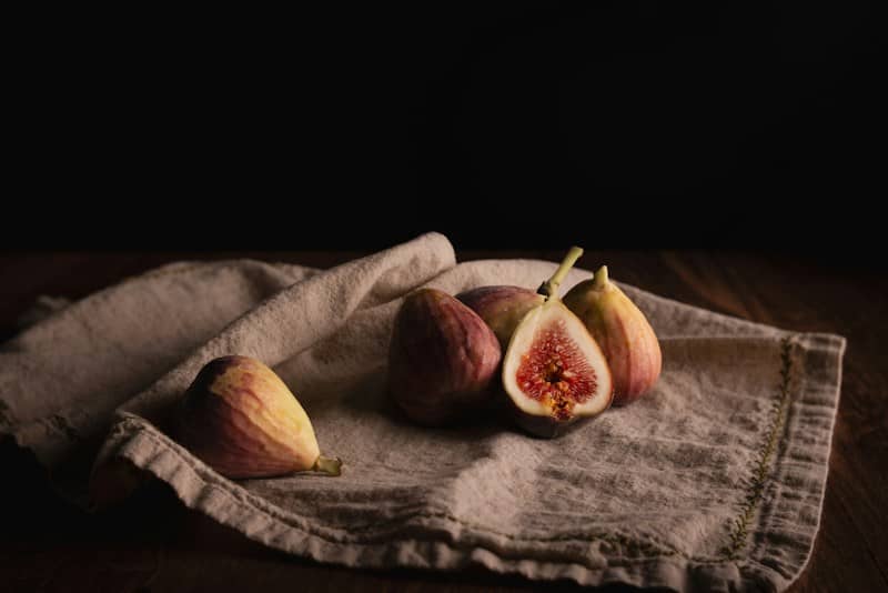 Whole and halved figs on a beige linen cloth against a dark background