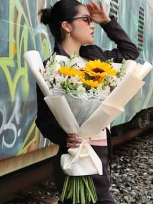 A woman in a pinstripe suit holding a sunflower bouquet beside a graffiti-covered train