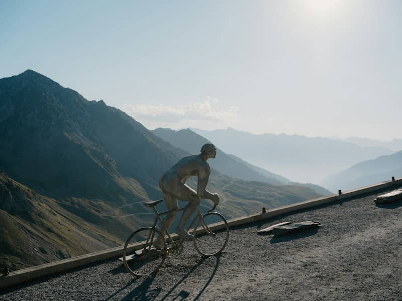 A metal sculpture of a cyclist on a mountain road with hazy peaks