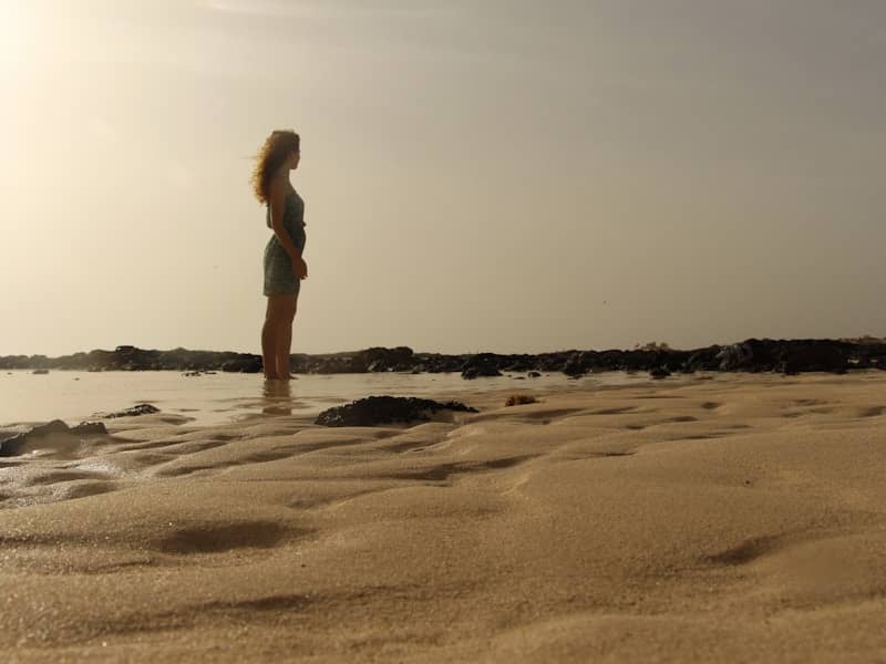 A woman with long curly hair in a dress on a sandy beach