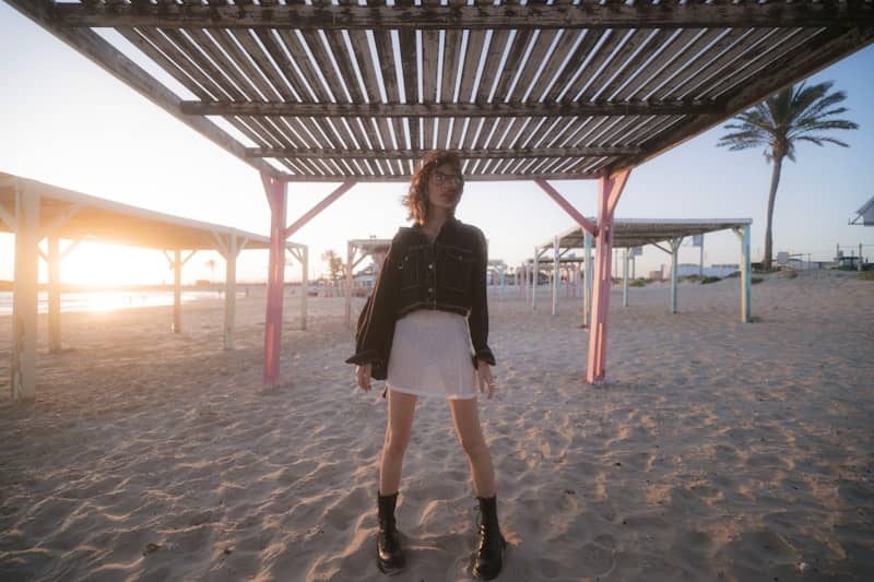 Woman under a pergola on a beach during sunset.