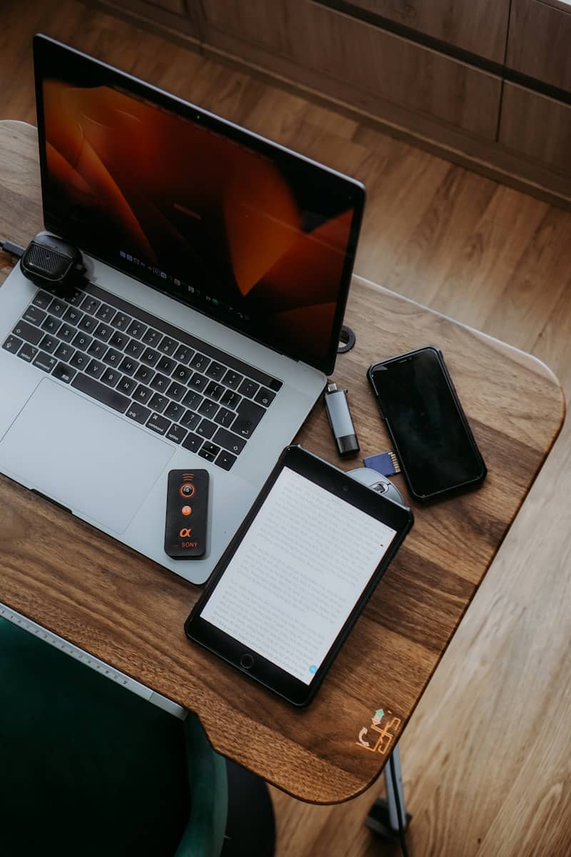 Laptop, tablet, and phone on a wooden desk.