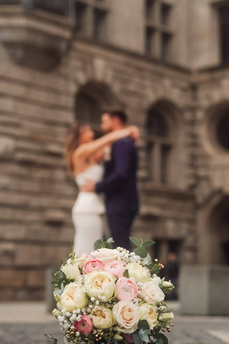 A bouquet of white and pink roses with a blurred couple in the background.