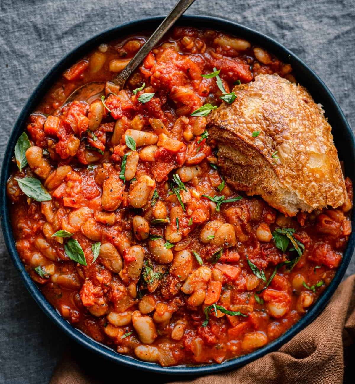 livornese stewed beans in a bowl bowl with a piece of bread on blue tablecloth