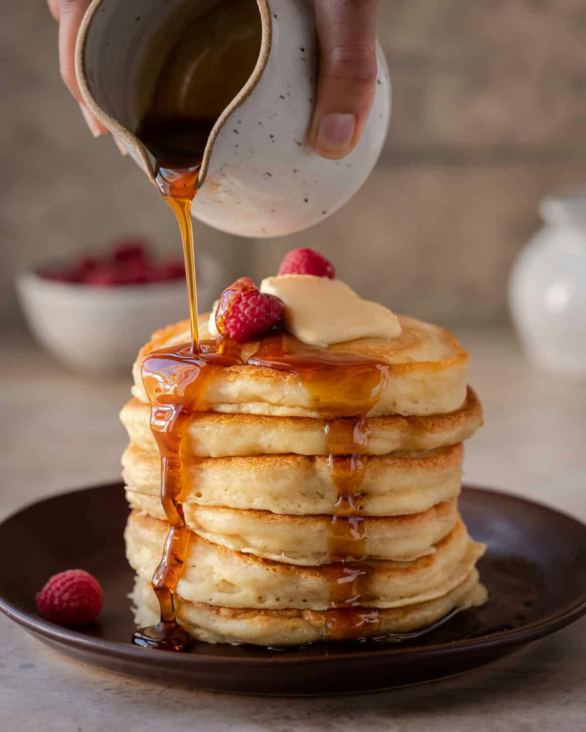 pouring maple syrup on a stack of vegan pancakes.