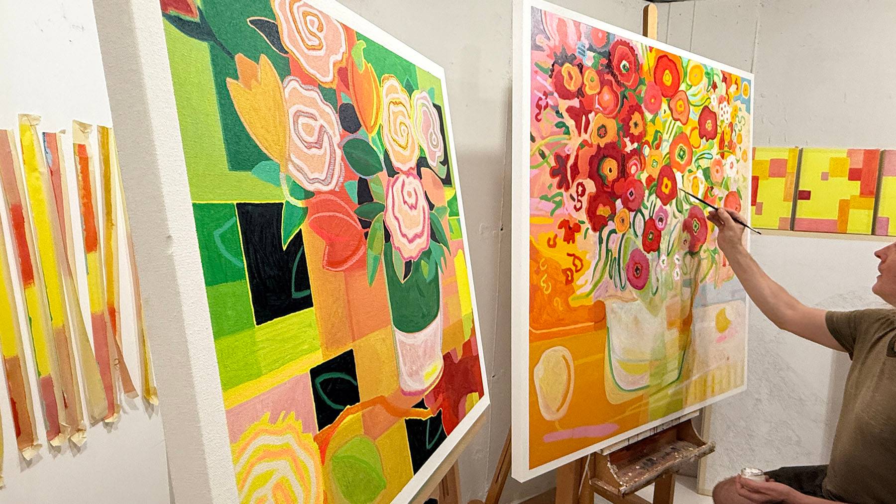 Two paintings sitting on easels with the artist putting the finishing touches to them