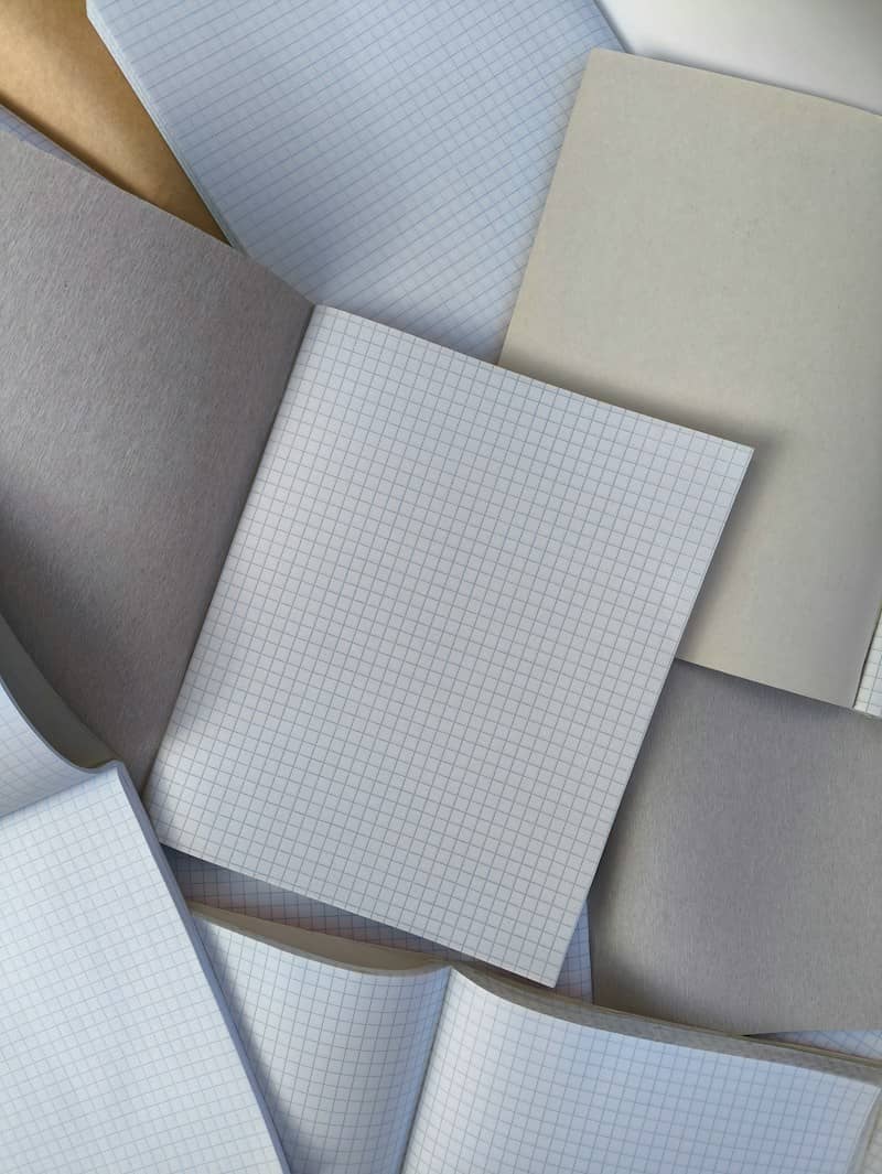 A collection of overlapping grid paper notebooks and plain grey paper sheets