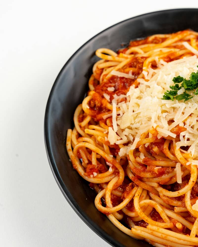Spaghetti with meat sauce topped with shredded cheese and parsley in a black bowl