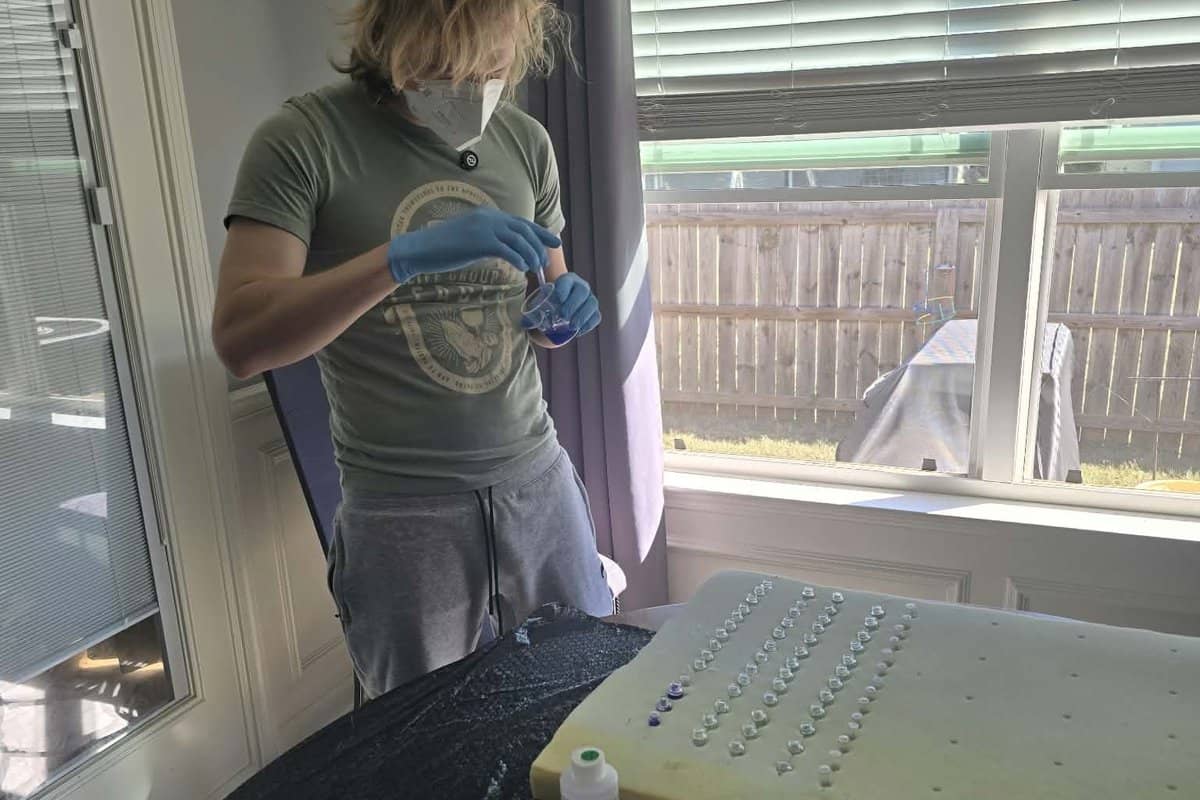 Robert in a mask and gloves pouring resin, with rows of tiny vials standing in foam on the table.