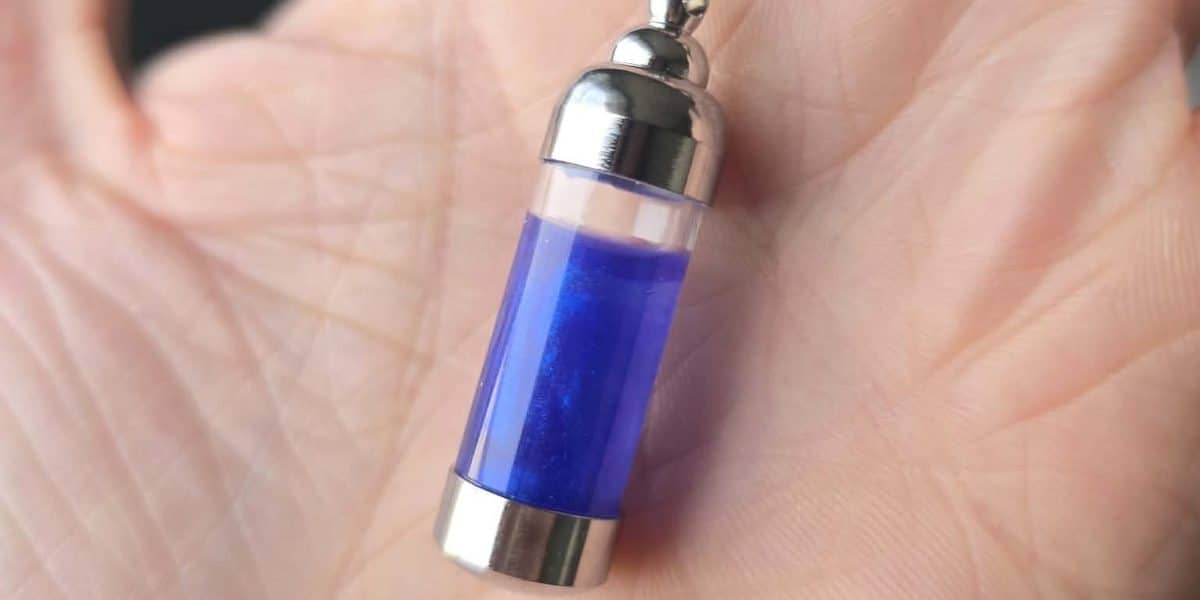 A small glass vial of glowing blue Pax Serum resting in an open palm.