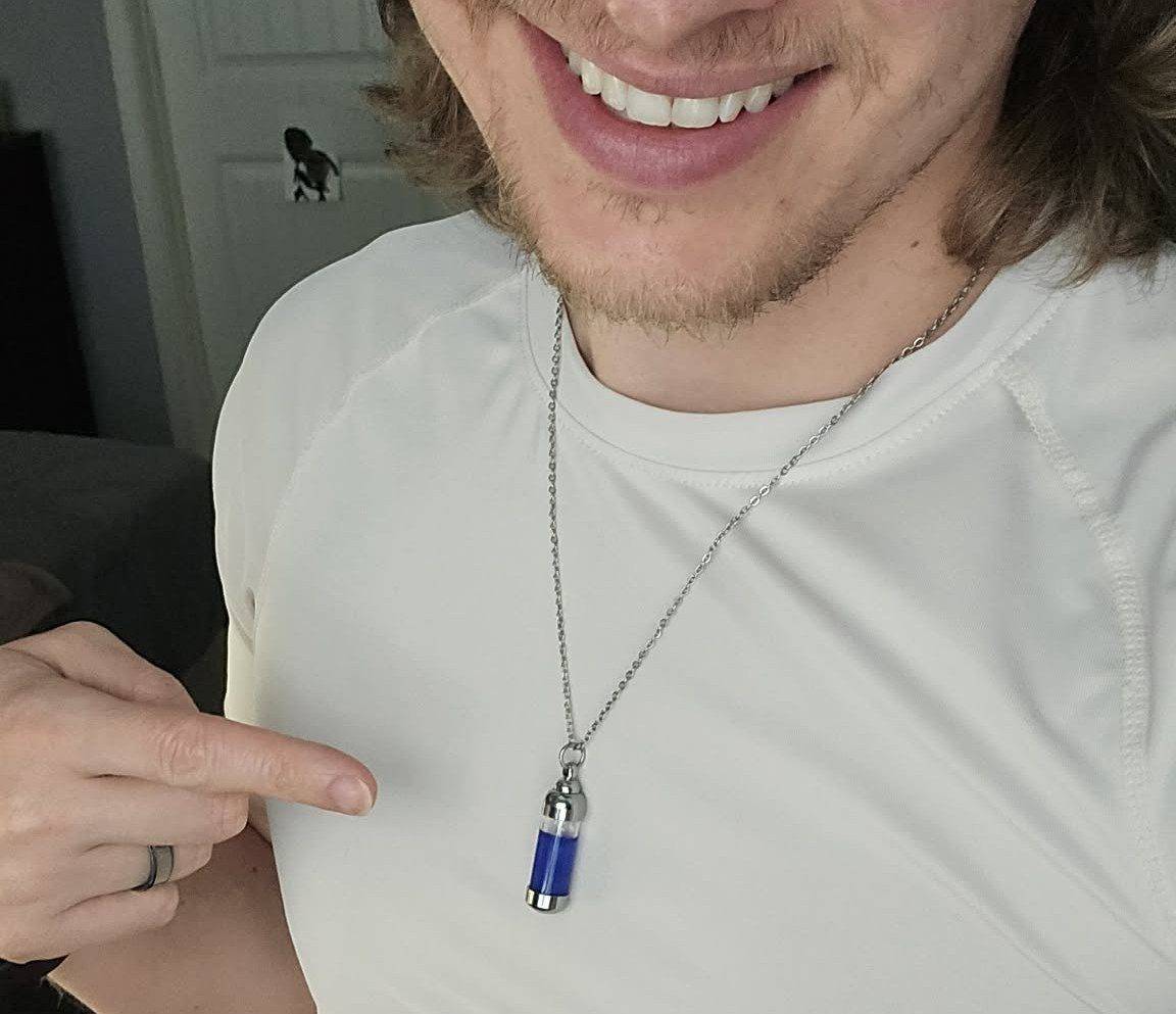 Robert smiling and pointing at the blue Pax Serum vial necklace he wears.