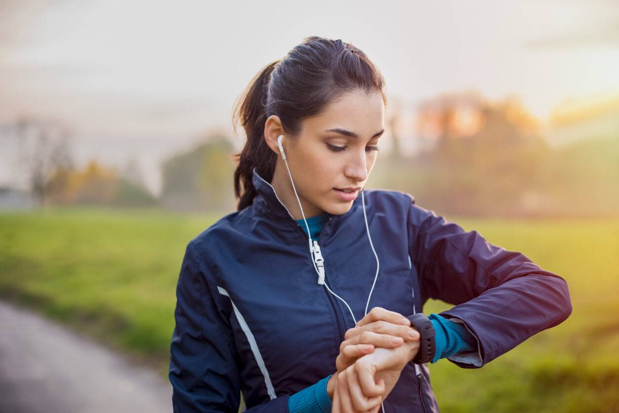 Runner, wearing headphones, preparing for an outdoor run by setting their fitness watch