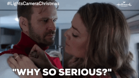 A woman playfully adjusts a man's red sweater while asking, "Why so serious?" A hashtag #LightsCameraChristmas and Hallmark Channel logo are visible at the top corners of the image.