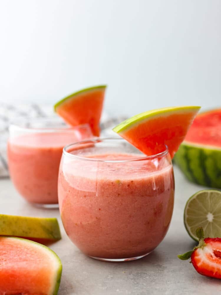 A watermelon smoothie in a glass cup with a slice of watermelon on the rim. 