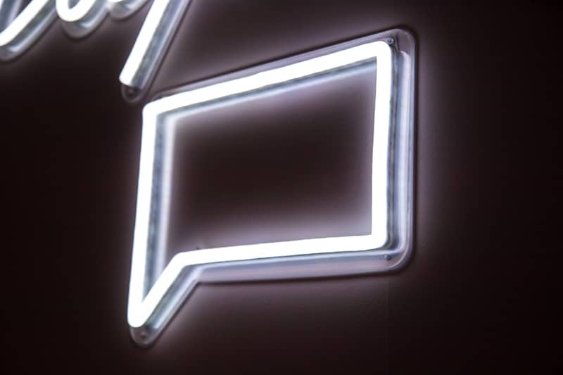 A speechbubble in white neon lights on a dark wall.