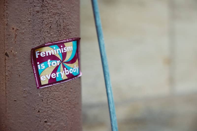 a sticker on a wall that says "Feminism is for everybody" over a swirly, colourful background