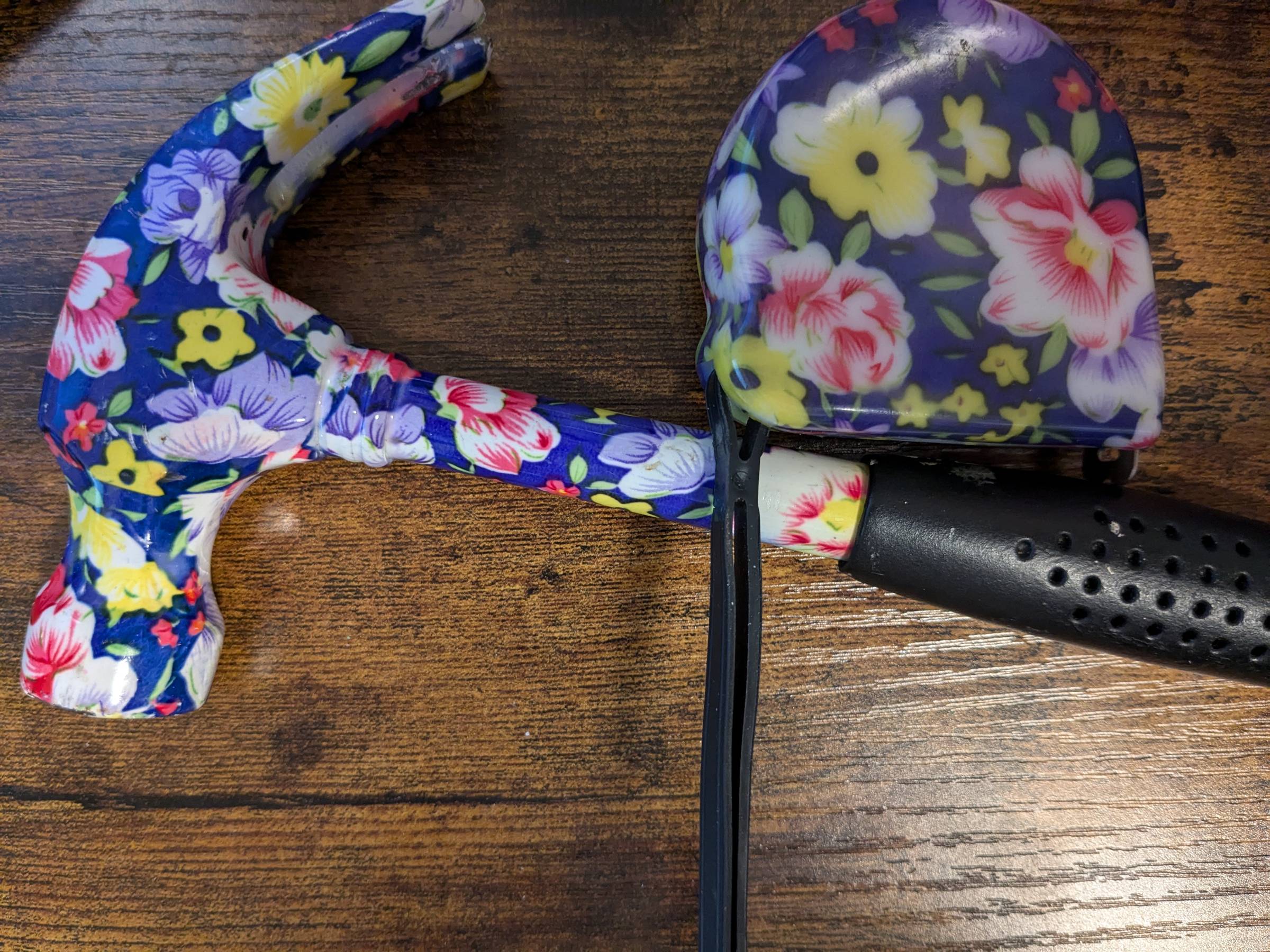 A wooden desk with a hammer and measuring tape on top. Both are adorned with blue, pink, periwinkle, yellow, and white flowers.