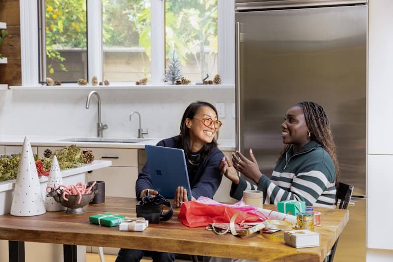 two people sitting at a table with a computer, smiling and talking animatedly