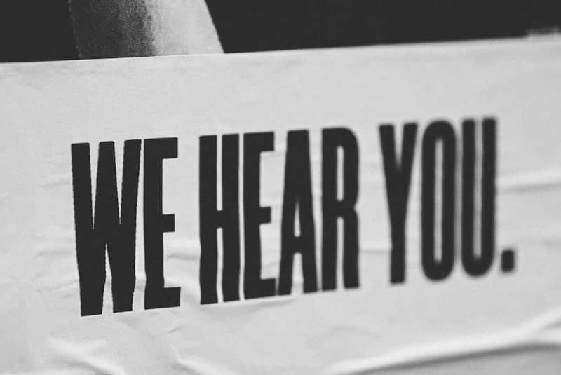 A black and white picture of a white sign with the words "We hear you." in black letters in all caps.