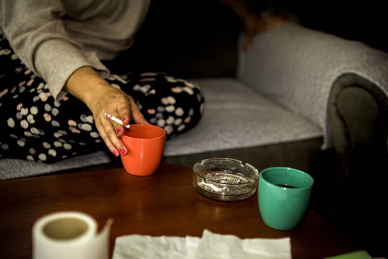 Person holding a cigarette, orange cup, with ashtray on table.