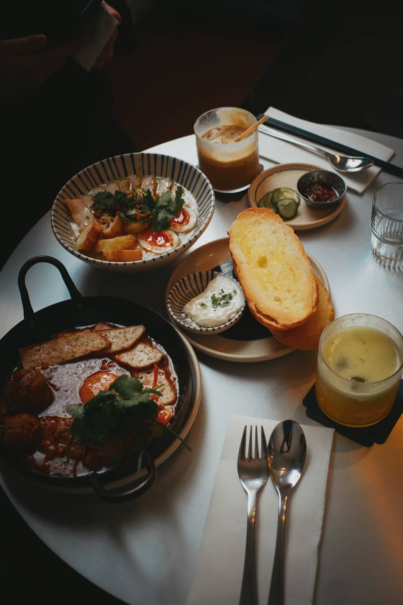 A bowl of congee with eggs and bread beside a skillet of breakfast food
