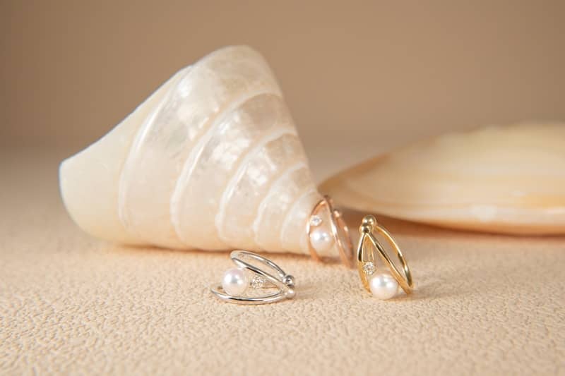 Pearl earrings rest next to a seashell.