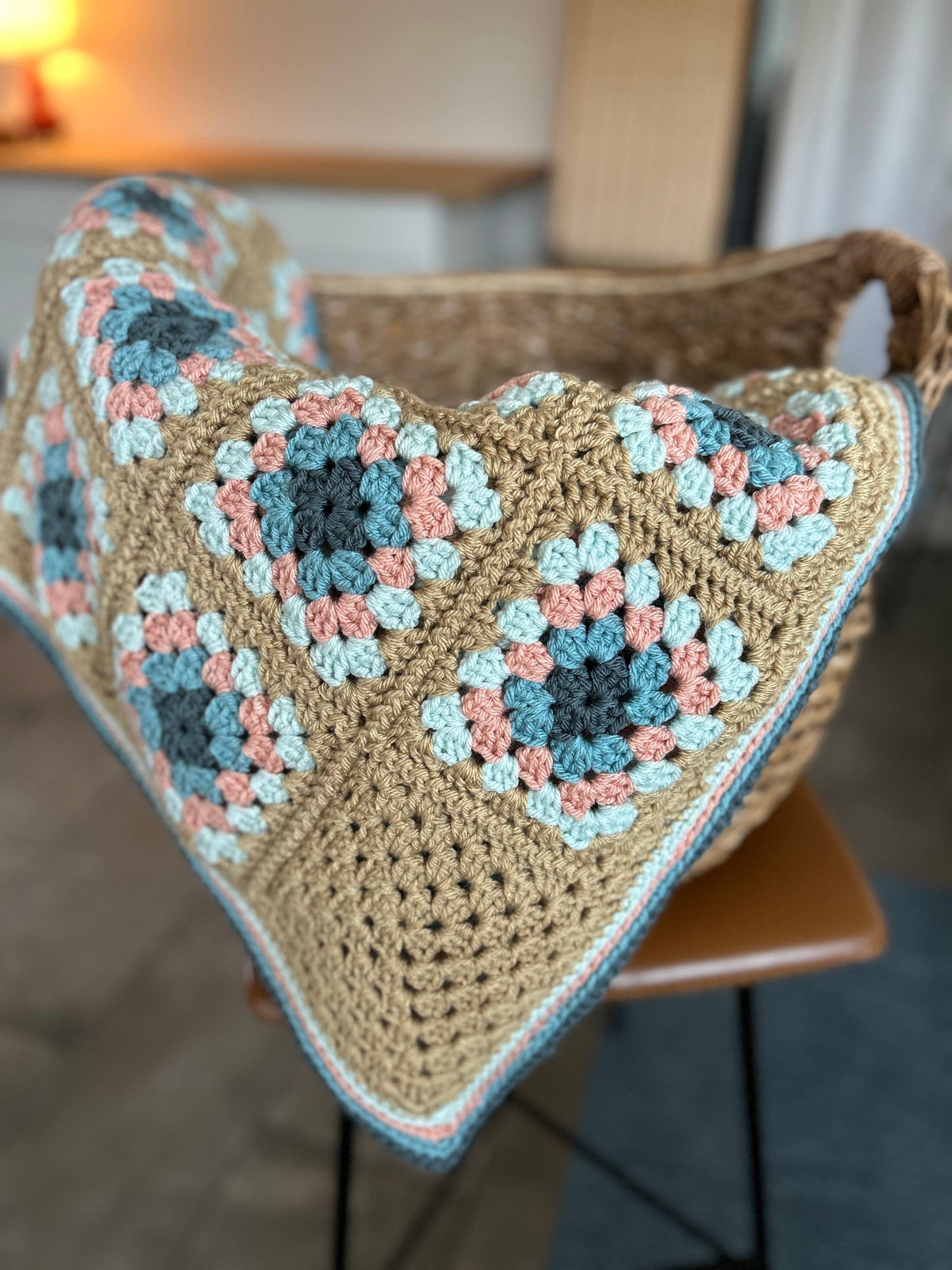 a Sea Glass and Sand crochet granny square blanket hanging out of a wicker basket