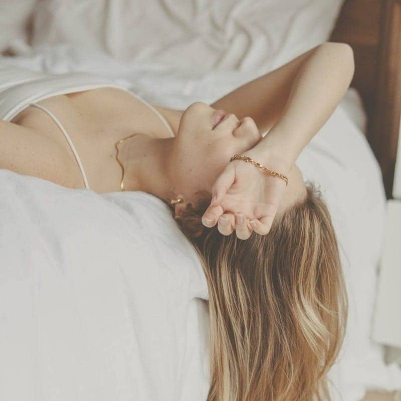 woman in white spaghetti strap top lying on bed