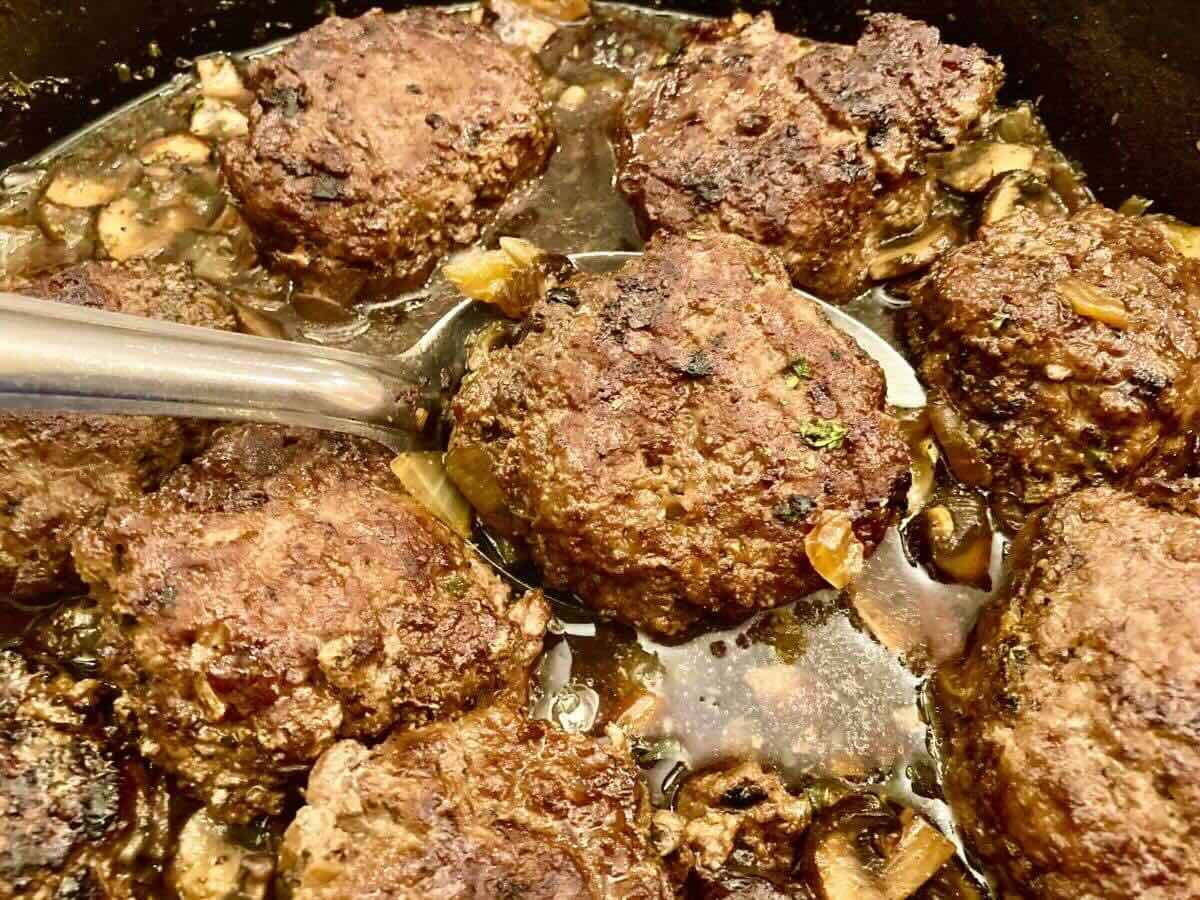 A spoon scooping Salisbury steak out of rich mushroom and onion gravy.