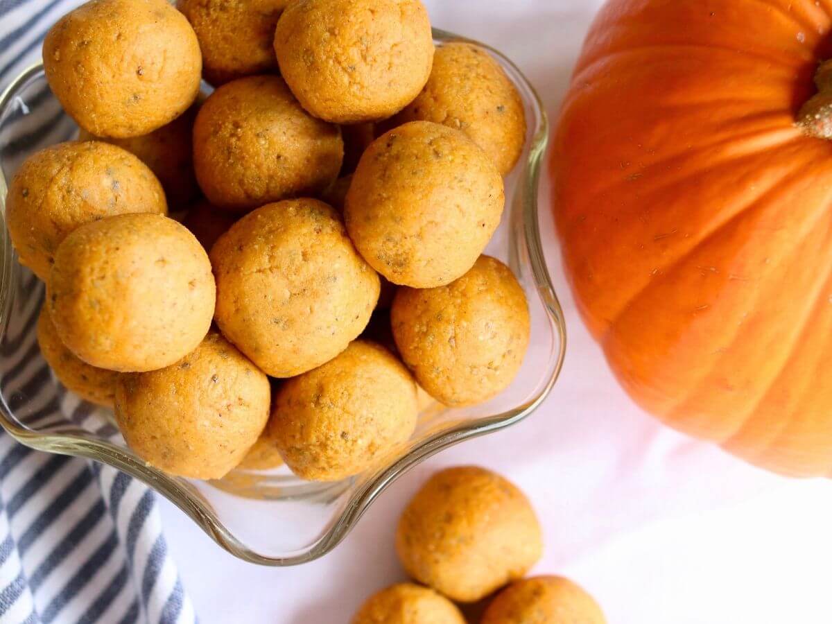 A glass dish of pumpkin protein balls beside a pumpkin. 