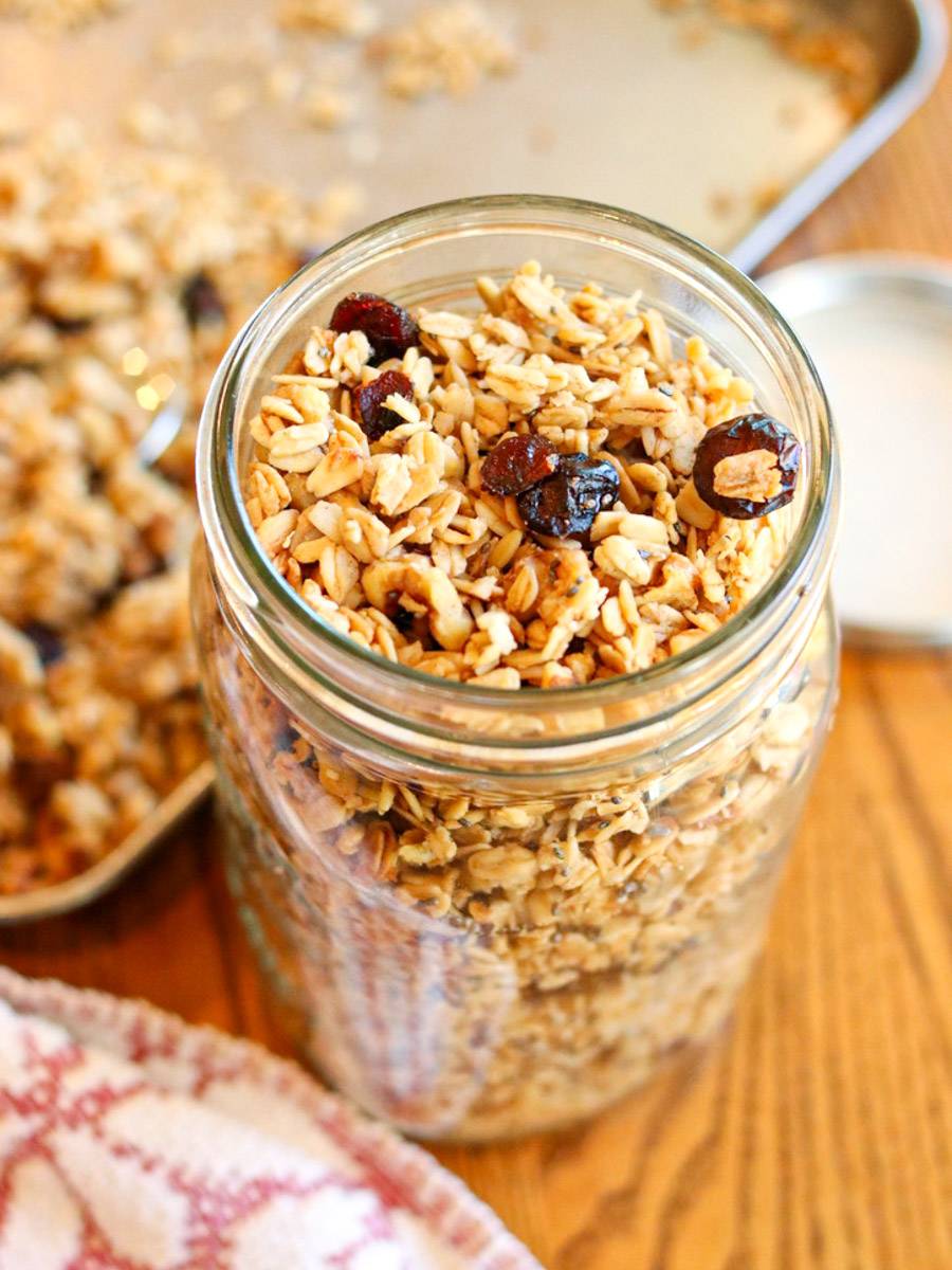 Homemade cinnamon granola in a glass jar with a baking sheet of granola in the background.