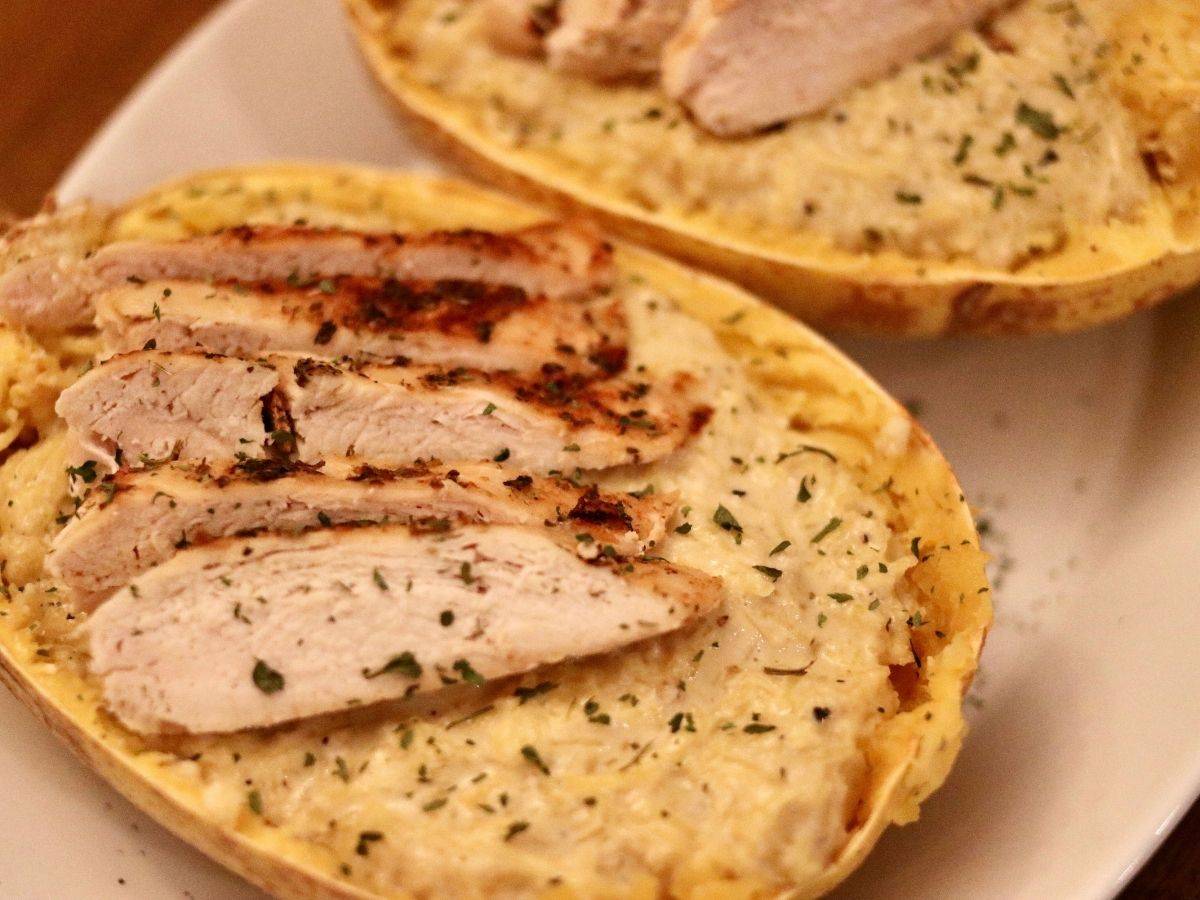 Spaghetti squash chicken Alfredo topped with sliced chicken on a white serving platter.