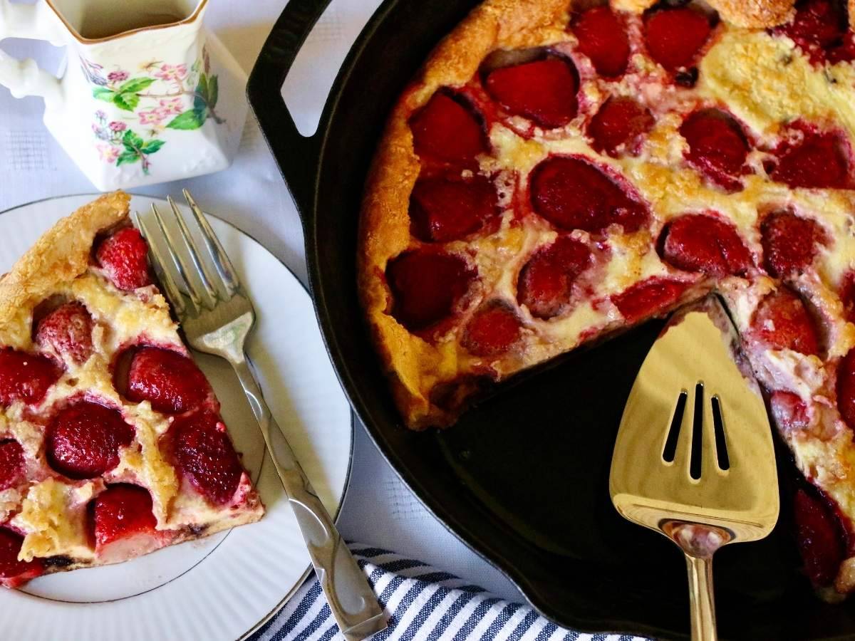 A strawberry Dutch baby in a cast iron skillet with a slice on a plate with a fork.