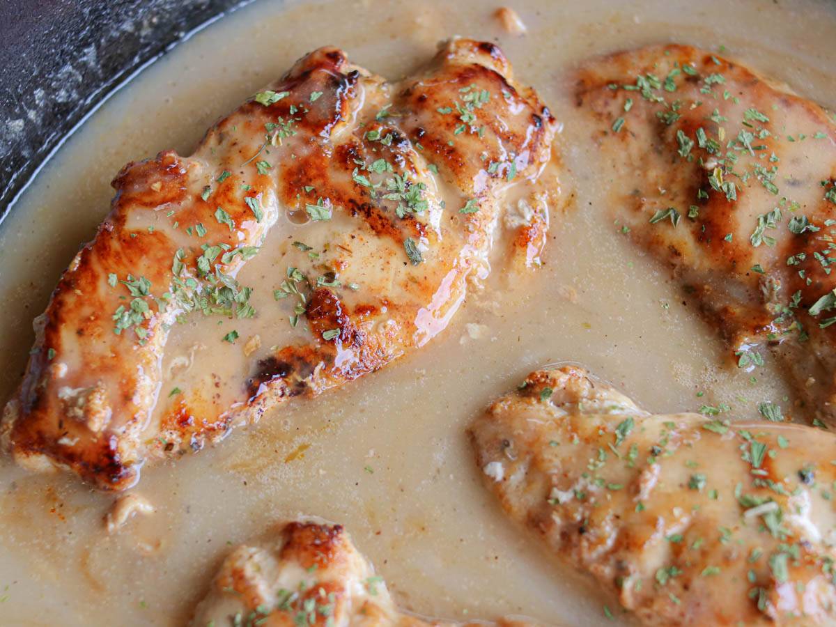 Chicken breasts in a cast iron skillet smothered in gravy.