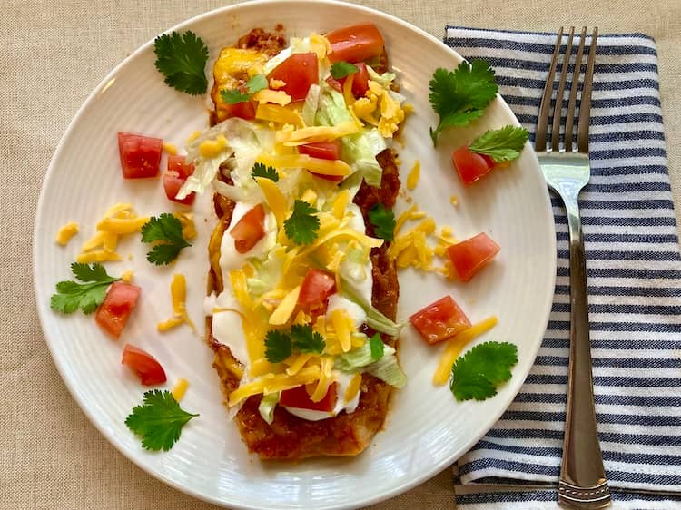 Chicken enchilada on a plate topped with sour cream, shredded cheese, chopped tomatoes, and fresh cilantro.