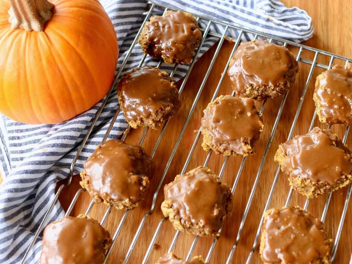 Glazed pumpkin cookies on a cooling rack beside a pumpkin.