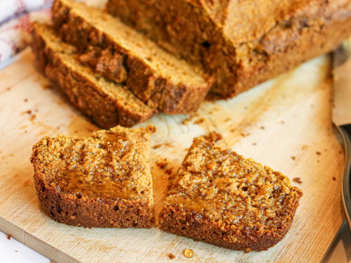 A halved slice of pumpkin banana bread drizzled with honey on a cutting board.