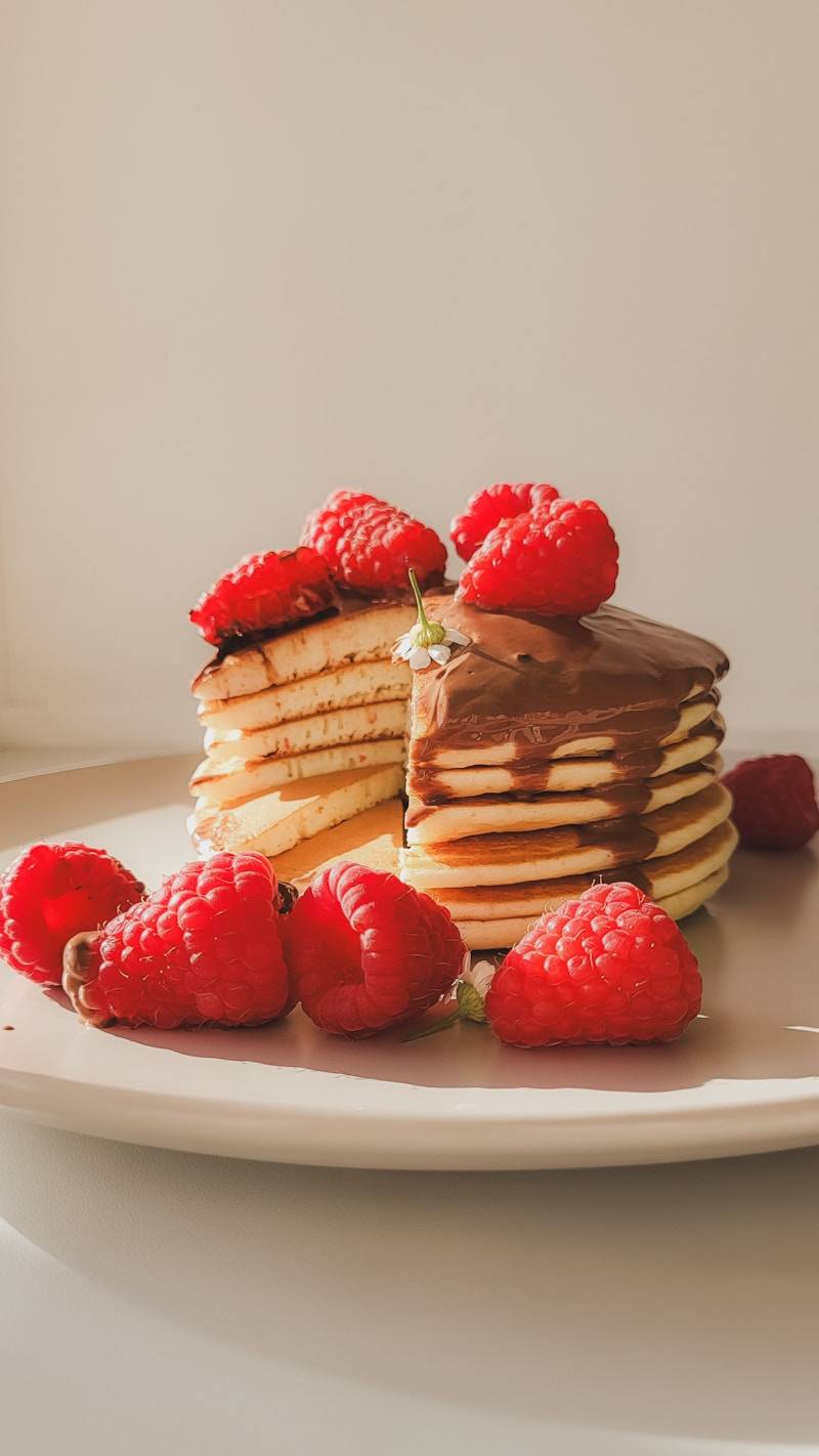 A stack of pancakes with raspberries on a plate