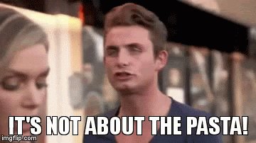 Reaction image from a TV scene showing a man speaking emphatically while a woman looks down beside him. Large white caption text across the bottom reads, “IT’S NOT ABOUT THE PASTA!”